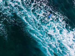 The surfer near his blue surfboard in the tropical blue ocean on the popular surf spot trying to catch a wave. Top view aerial drone landscape, Bali, Indonesia.