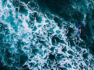 The surfer woman moving around on surfboard in the tropical blue ocean on the popular surf spot trying to catch a wave. Top view aerial drone landscape, Bali, Indonesia.