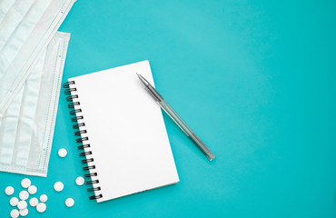 Notepad with free space for writing on a turquoise background and protective masks, pills.