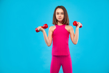 Kid girl doing fitness exercises with dumbbells on blue background