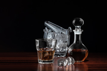 Obraz na płótnie Canvas Crystal decanter or carafe of whiskey and glass with alcoholic drink and ice bucket on wooden table in restaurant. Black background for copy space