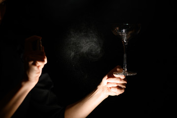 close-up bartender's hand holds empty transparent glass and spray to it