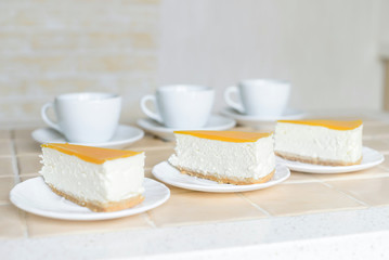 Three cheesecakes and three white cups on the table.