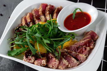 Delicious appetizer with sliced bacon, arugula, orange and red sauce on grey table. Traditional dish menu served in a restaurant, close-up