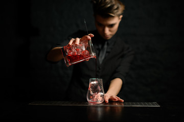 female bartender gently pours cocktail from mixing cup with strainer into glass of ice