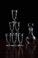 Crystal decanter or carafe of vodka and glasses pyramid tower on wooden table in restaurant, black background