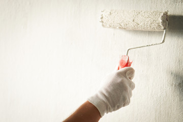 Detail of a painter who is painting walls in a room on white colour.