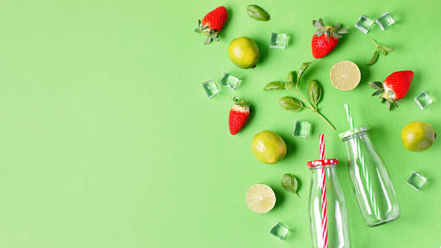 Flat lay with ingredients for summer refreshing drink or smoothie, ice cubes, herbs and glass jars on green background, top view. Strawberry, lime, ice and basil for delicious summer cocktail - Powered by Adobe
