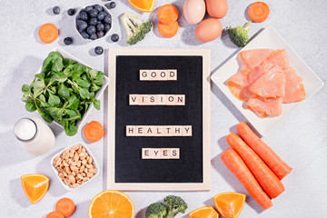 Foods that help maintain eyes healthy, products for keeping good vision, vitamins for eyes. Black board with copy space, assortment of food for eye health on concrete background, flat lay, top view