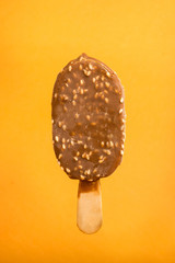 chocolate ice cream with sesame on a stick on a yellow background