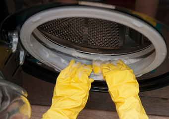Female hands in yellow latex gloves for cleaning with a sponge wash the dirt around the drum of a black washing machine