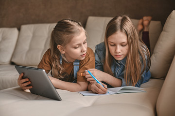 Two beautiful sisters do their homework during quarantine. Children use gadgets for learning. Education, distance learning, home schooling during quarantine