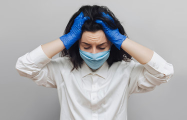 Young nurse doctor in a protective blue medical mask holds his head in his hands. Physical fatigue,...