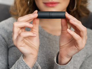 Woman's beauty blogger hands holding professional hi-end cosmetic lipstick with blurred body background, warm cozy tones and copyspace