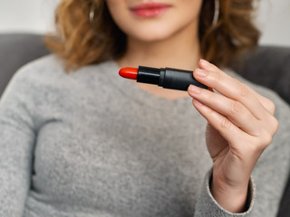 Woman's beauty blogger hands holding professional hi-end red lipstick with blurred body background,...