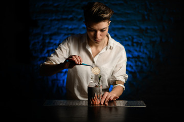 Woman bartender accurate decorates figured glass with ice by slice of citrus using tweezers and...