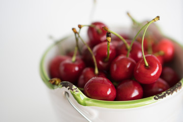 Ripe red cherry in a white garden enamel bucket with a green border on a white background close-up