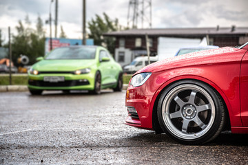 The front of a red sports tuned car with lowered suspension. Against the background of another...