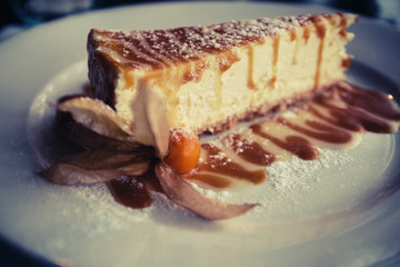 Honey cheesecake with chocolate icing in icing sugar lies on a white plate in a cafe.