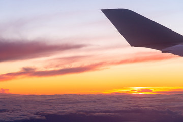 Airplane flight. Wing of an airplane flying above the clouds with sunset sky. View from the window of the plane. Colorful sunset above clouds. Aircraft. Traveling by air. Space for text