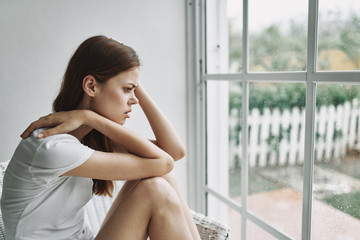 Naklejka na ściany i meble sad young woman sitting on the windowsill