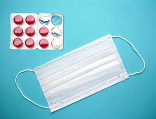Medical disposable face mask and red candies for the throat on isolated on a blue background.