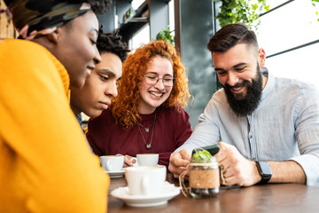 Four friends watching something on the phone in the cafe.