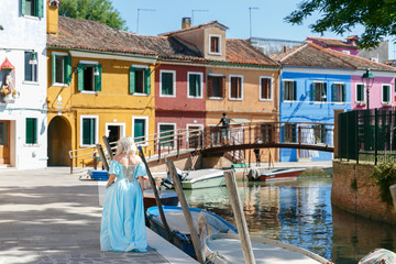a blonde in a blue dress walks the streets of the island of Burano in Venice. Dancing girl walking among colorful houses