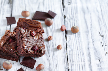Fresh made homemade brownies made with from chocolate candy and hazelnuts over a a white rustic...