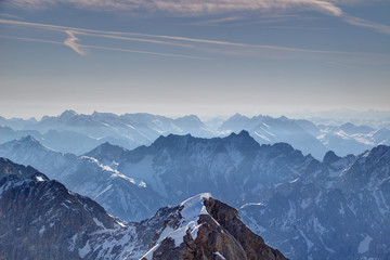 Elevated view of jagged ridges and snowy peaks in morning haze under blue sky with clouds and contrails, Wetterstein and Karwendel mountains Bavarian Alps Northern Limestone Alps Bayern Germany Europe