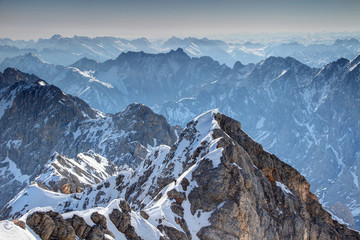 Elevated view of snowy climbing route Jubilaumsgrat with tiny climber ascending narrow rocky ridge in Wetterstein mountain with hazy Karwendel range in background, Bavarian Alps Bayern Germany Europe