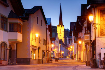 Empty main street in blue hour in historic center of Bavarian resort town Garmisch-Partenkirchen with spire of Maria Himmelfahrt church above row of traditional German houses, Bayern Germany Europe