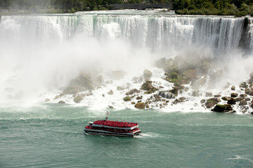 Obraz premium Niagara Falls tour boat red rain suits waterfall. Waterfalls at border of US state of New York and Canadian province of Ontario. Drains Lake Erie into Lake Ontario. 