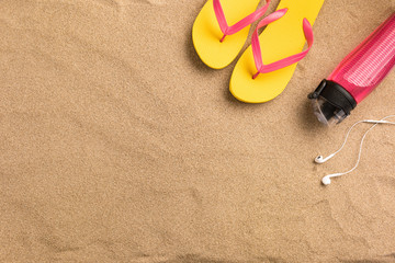 Fototapeta na wymiar Top view flip flops and headphones with copy space. Traveler accessories on sand. Travel vacation concept. Summer background. Border composition made of towel