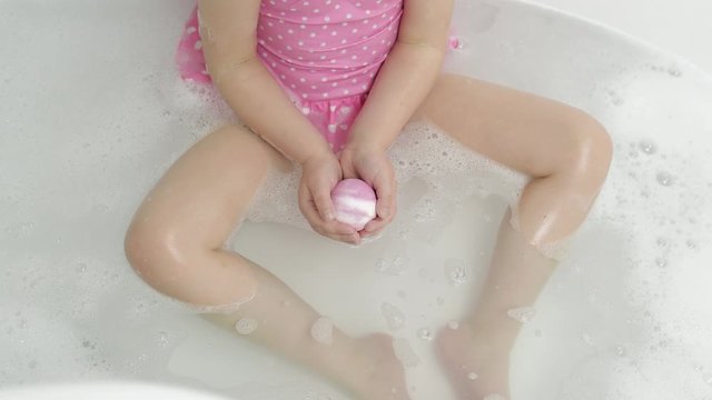 Hands of girl puts bath bomb to water. Ball of bath salt dissolves in water