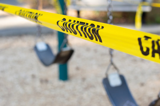 Yellow caution tape closing swings in a city park.