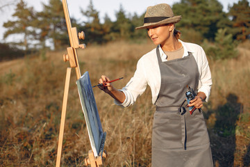 Woman in a summer field. Lady drawing. Woman in a apron and hat.