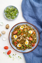 Mung bean porridge with quail eggs, tomatoes and microgreen sprouts on a white concrete background. Top view, close up.