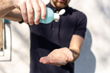 Hand sanitizer alcohol gel rub clean hands hygiene prevention of coronavirus virus outbreak. Man using bottle of antibacterial sanitiser soap. Outside on the street with sunshine and shadows