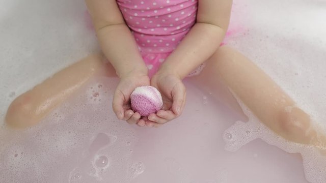 Hands of girl puts bath bomb to water. Ball of bath salt dissolves in water