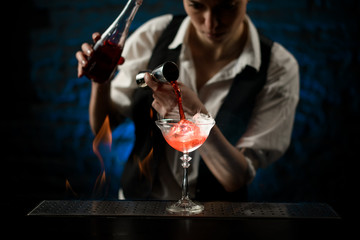 bartender masterly pours drink into glass at dark bar