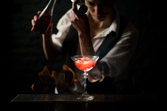 professional bartender masterly pours drink into glass at dark bar.