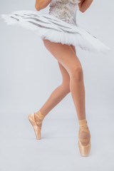 Professional legs of a young ballerina who puts on pointe shoes isolated on a white background in the studio. Ballet practice. Beautiful slim graceful legs of a ballet dancer.