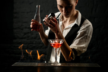 bartender professionally pours drink into glass which standing on burning bar counter