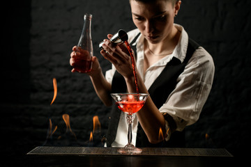 female bartender professionally pours drink into glass which standing on burning bar counter