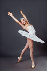 Classical Ballet dancer portrait. Beautiful graceful ballerina in white tutu from Swan lake practices releve ballet position in the studio. Vertical image of gifted young teenager in pointe on hippies