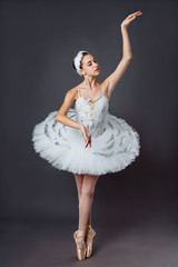 Naklejka premium Ballerina dancing in white dress. Color photo. Graceful ballet dancer or classic ballerina dancing isolated on grey studio background. Ballerina on point shoes feet tutu from Lake Swan