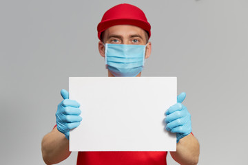 Courier in red uniform, protective mask and gloves Holding a white sign for text. Delivery service under quarantine.