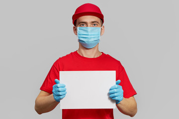 Courier in red uniform, protective mask and gloves Holding a white sign for text. Delivery service under quarantine.