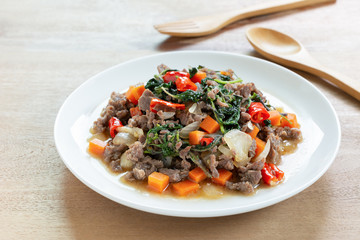 close up of stir fried minced beef with holy basil in a ceramic dish on wooden table. hot and spicy thai style food menu.